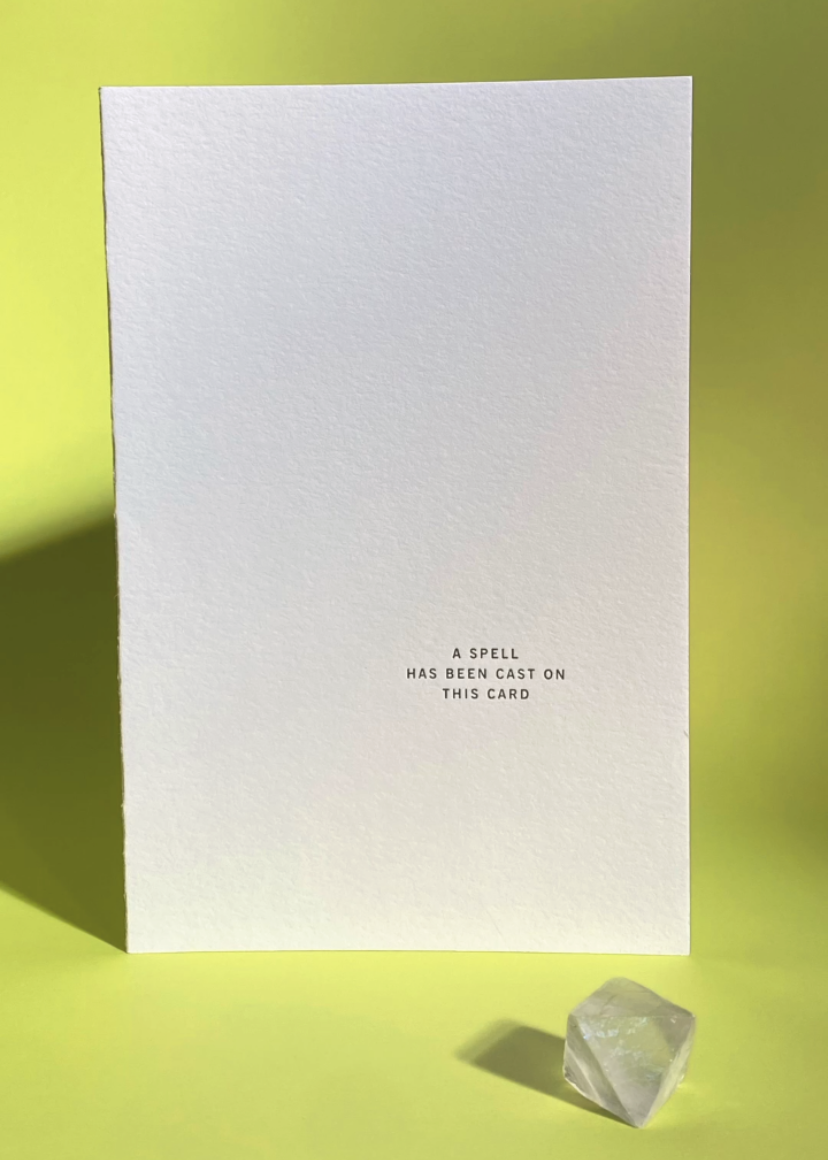 White card with the words A cspell has been cast on this card, and inside It's already working on you text on a lime green background with crystal