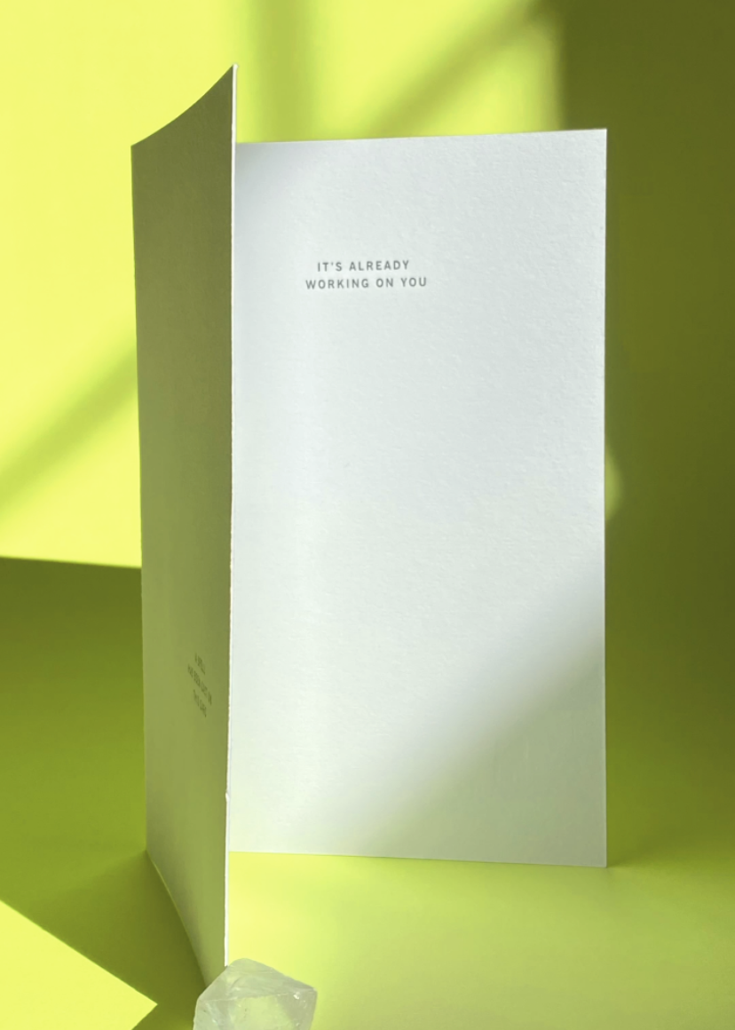 White card with the words A cspell has been cast on this card, and inside It's already working on you text on a lime green background with crystal