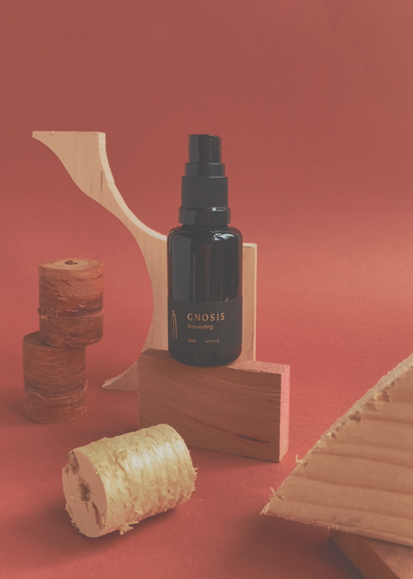 Noat_Celestial_Atmosphere_Gnosis_with_cedarwods_sandalwood_bergamot_clove on a deep red background with cut wood piece in a black glass bottle