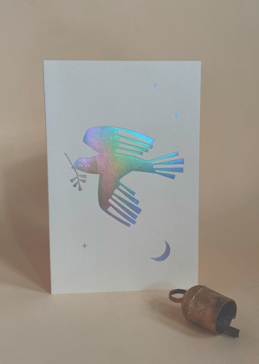 Peace on earth holiday greeting Card with an iridescent three eyed dove foil printed design on a peach background with rustic Christmas bell.